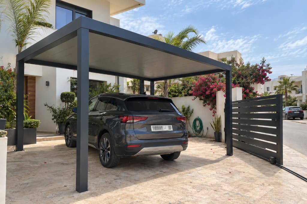 Carport aluminium anthracite devant une villa, une place, toiture pleine et portail à lames.