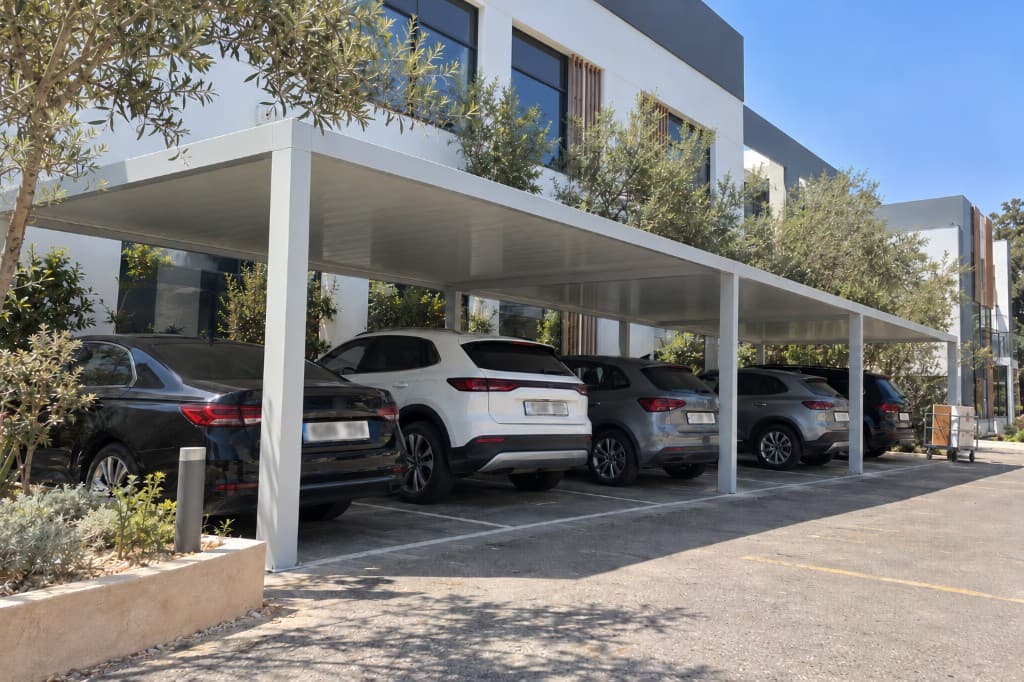 Carport aluminium en ligne, plusieurs véhicules garés devant un bâtiment.