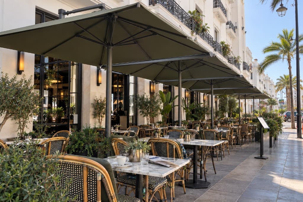 Parasols carrés verts en linéaire devant une façade de café, tables sur le trottoir.