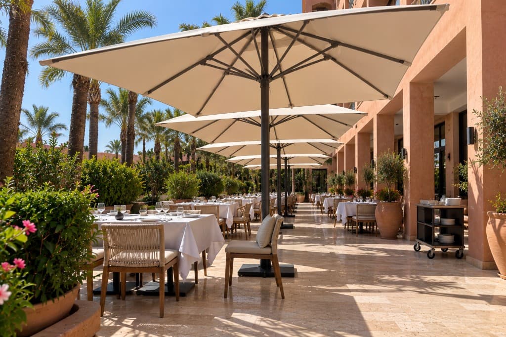 Rangée de grands parasols à mât central le long d'une terrasse de restaurant, passage de service dégagé.