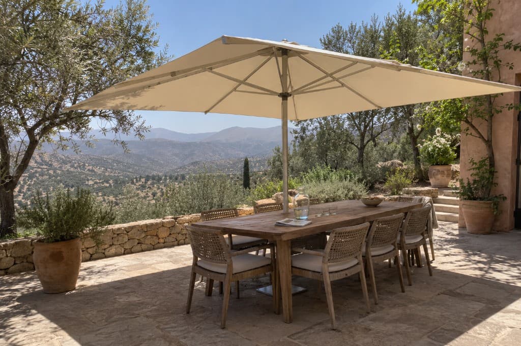 Parasol carré à mât central, toile claire, au-dessus d'une table dressée sur une terrasse.
