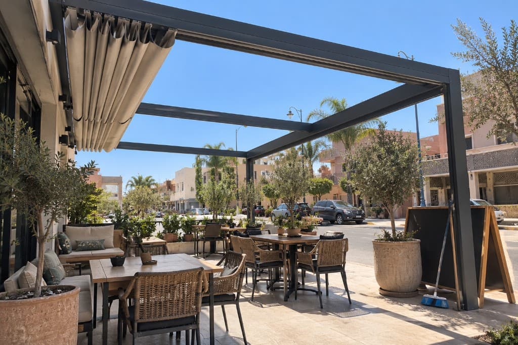Structure de pergola en façade de café, toile repliée sur un tronçon et ciel ouvert sur le suivant.